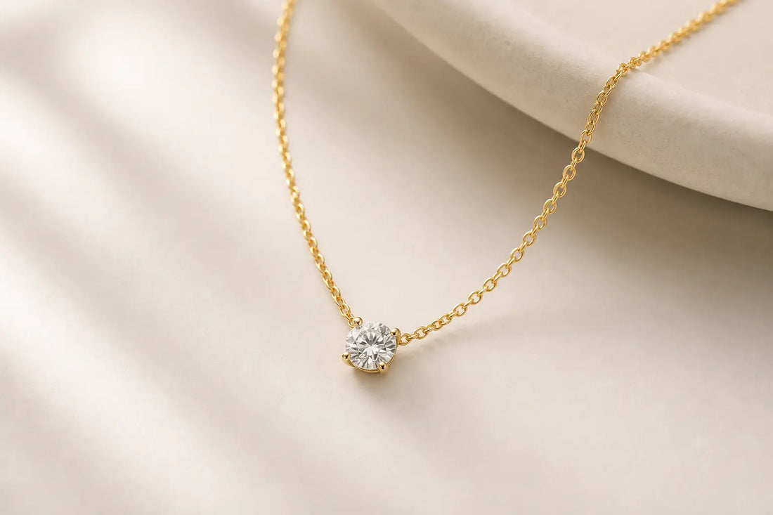 Simple diamond pendant necklace on a gold chain against a neutral background