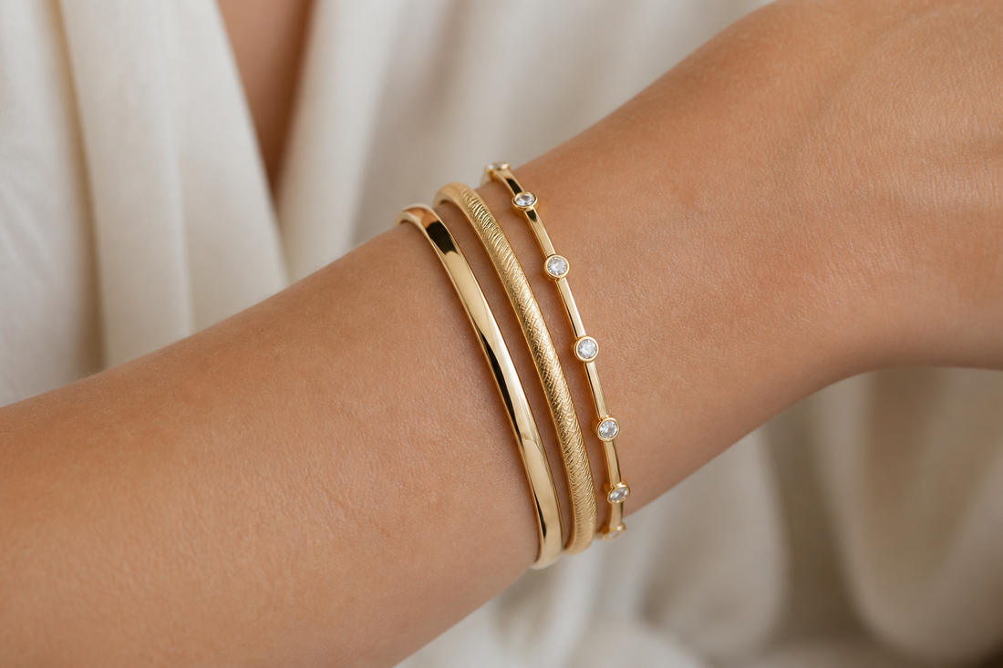 Close-up of a wrist wearing a stack of gold bangles with one plain, one textured, and one diamond accent style