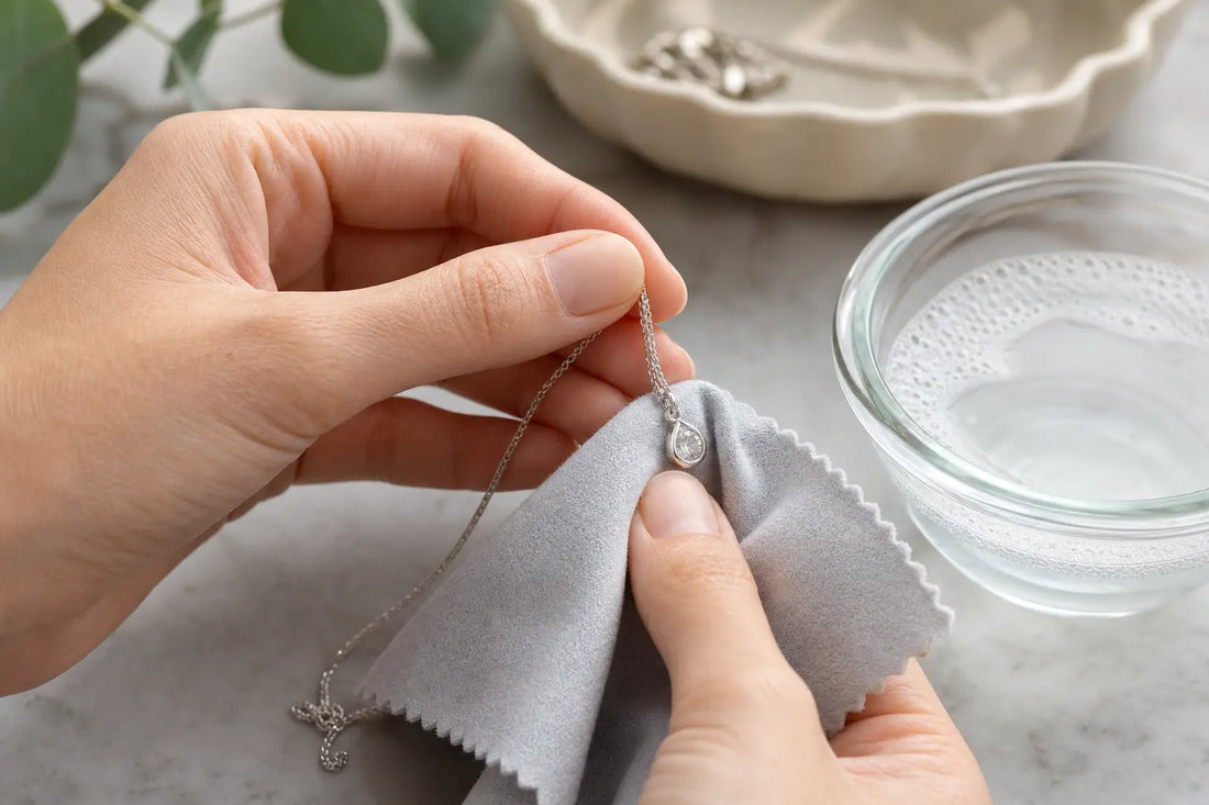 Hands cleaning a sterling silver necklace with a soft cloth next to a bowl of soapy water