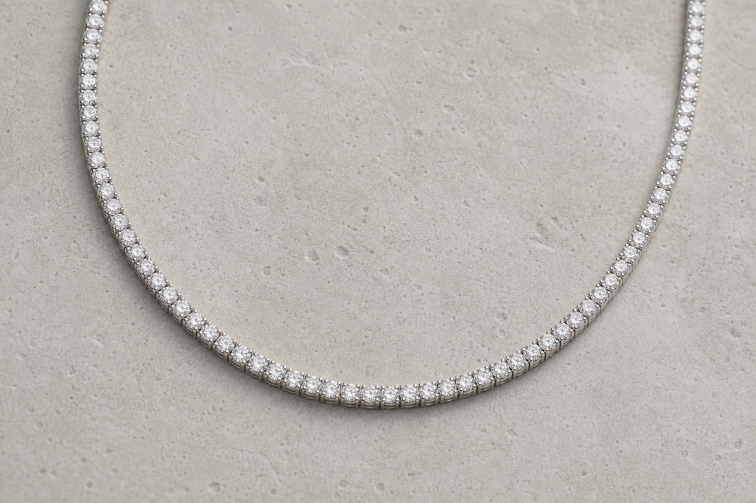 A diamond tennis necklace arranged in a soft curve on a neutral surface.